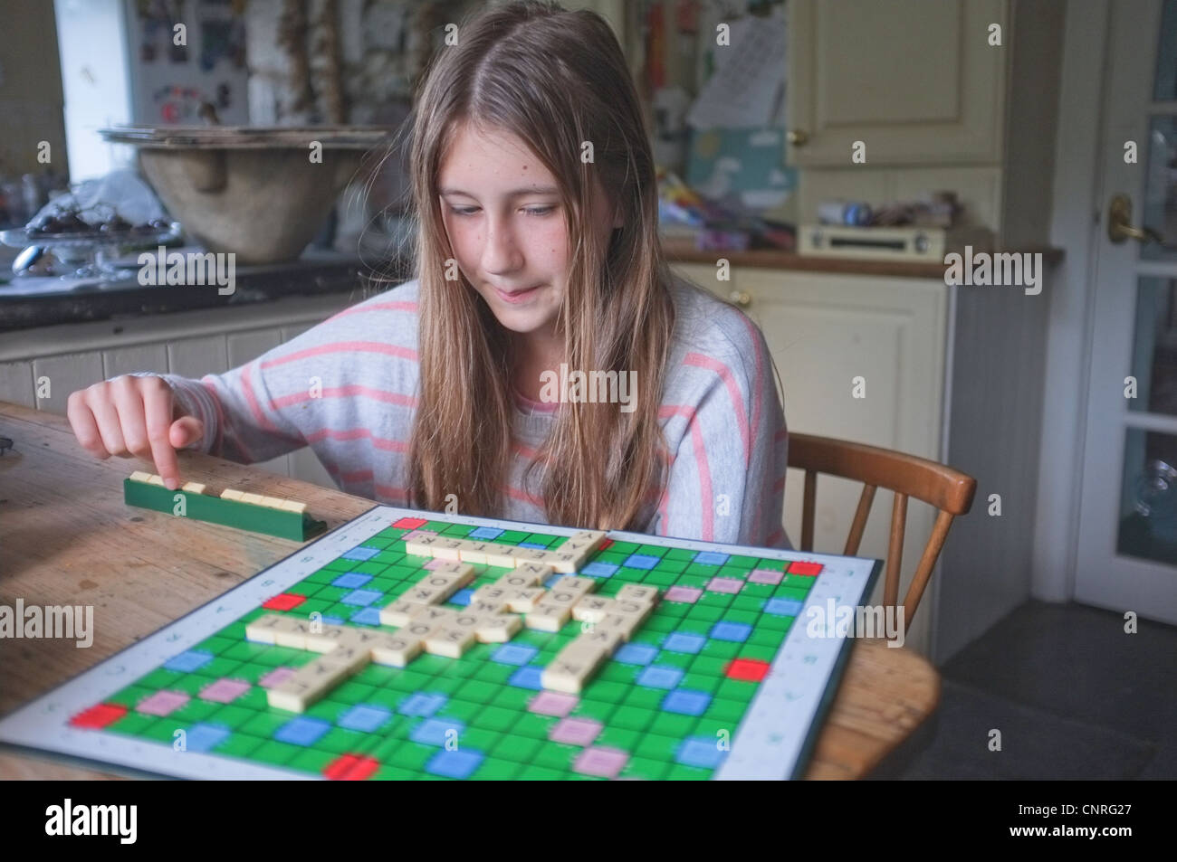 Una niña de 11 años de edad jugando Scrabble en una cocina Foto de stock