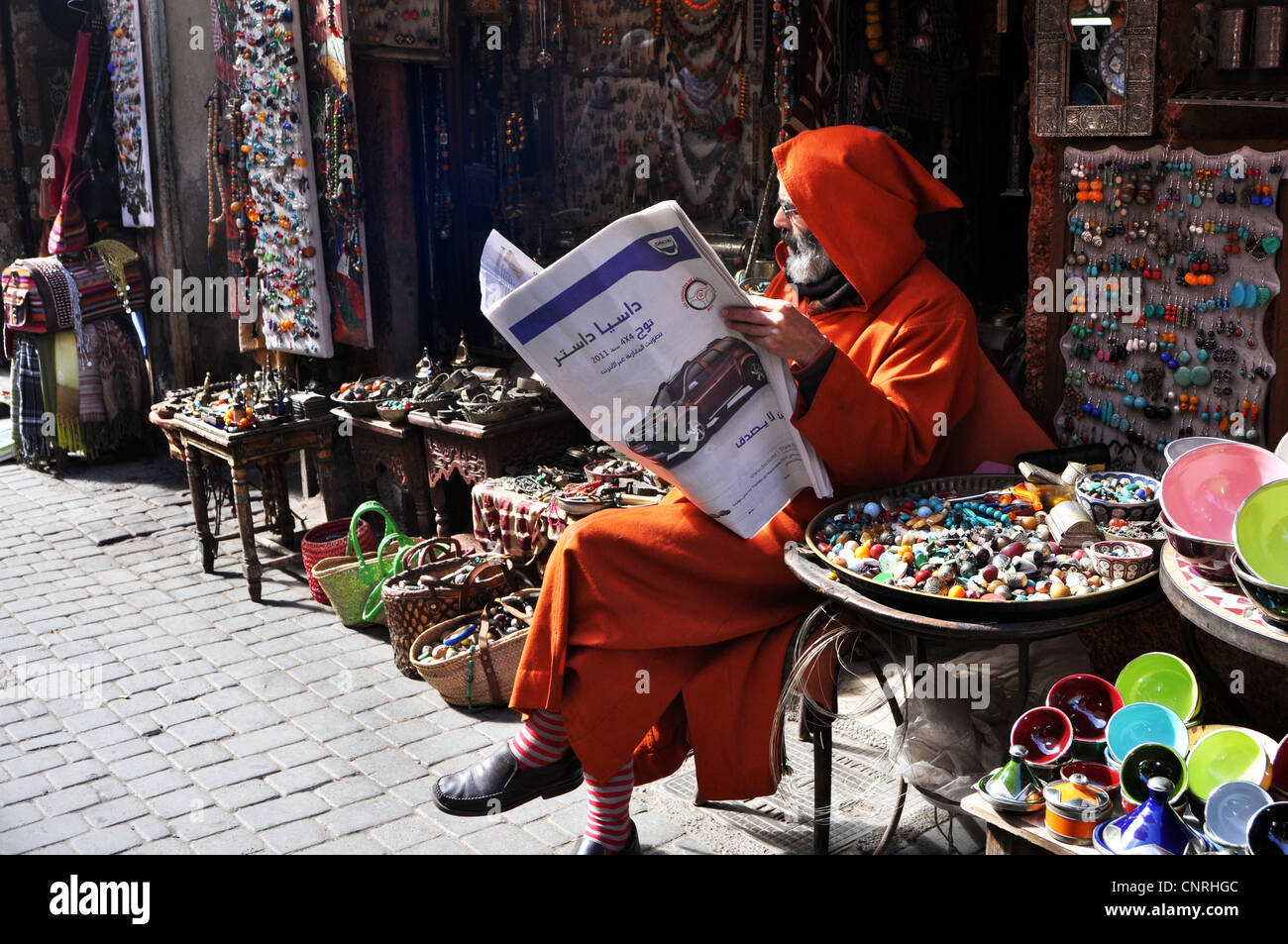 Un hombre bereber en vestimentas tradicionales lee un periódico, Marrakech, Marruecos Foto de stock