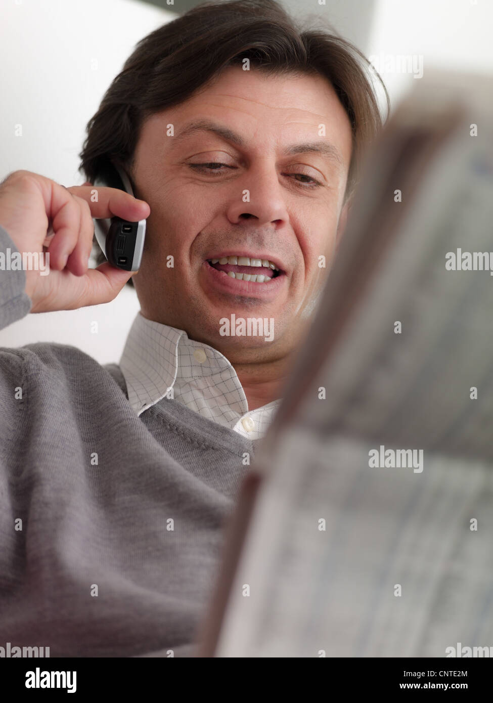Un varón de mediana edad Leyendo listas de valores y el comercio en el teléfono de casa. Foto de stock