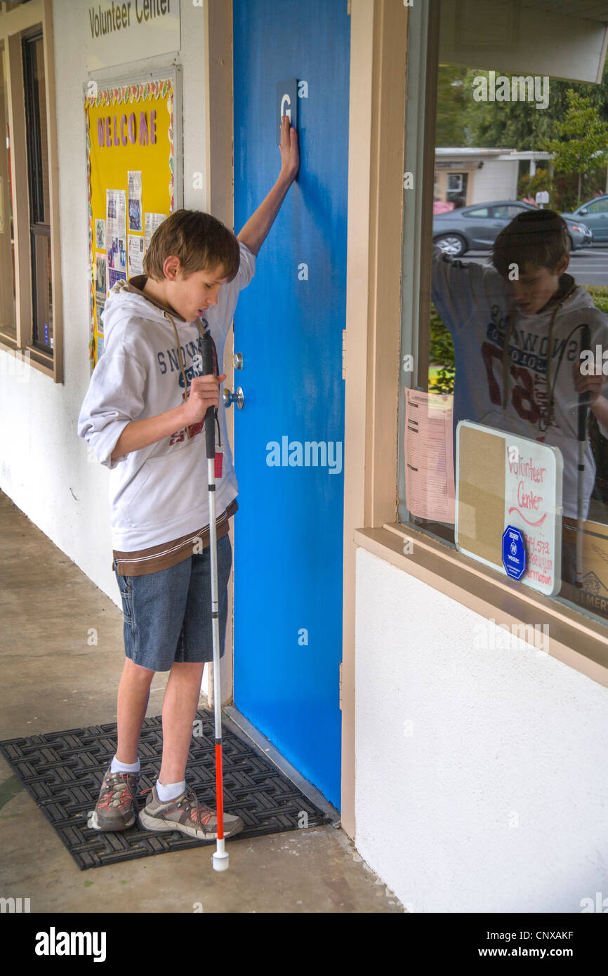Cantar un bastón blanco además de tocar, un muchacho preadolescentes encuentra su camino en el centro de aprendizaje para niños ciegos en Santa Ana, CA. Foto de stock