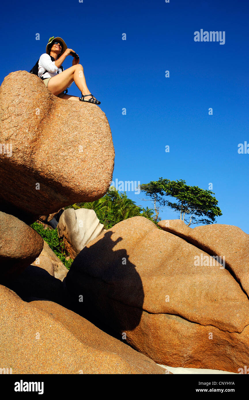 Mujer sentada sobre rocas de granito en la playa de Petite Anse, Seychelles, La Digue Foto de stock