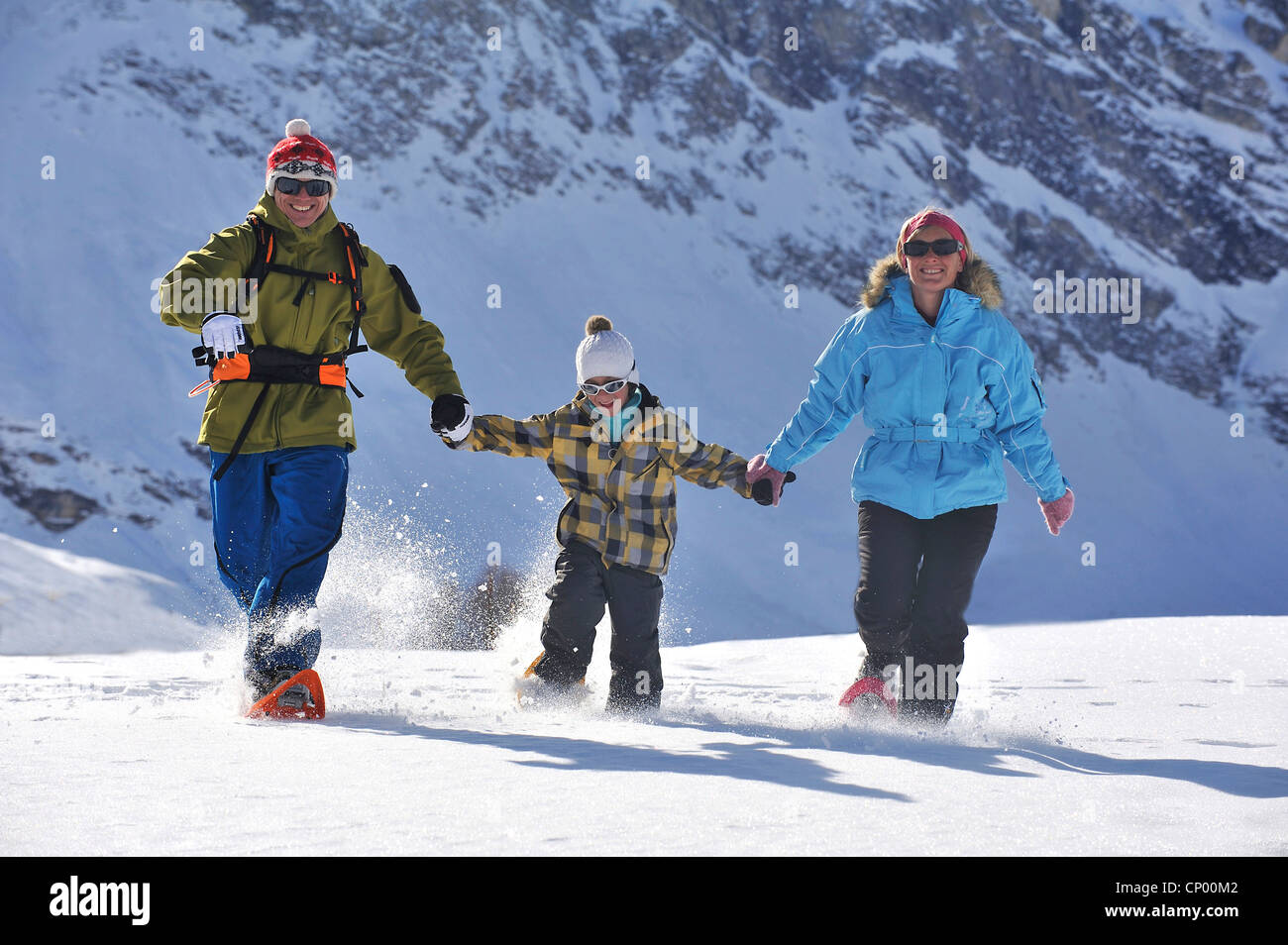 Familia en vacaciones de invierno caminando felices a través de un paisaje de montañas nevadas de la mano con zapatos de nieve, Francia Foto de stock