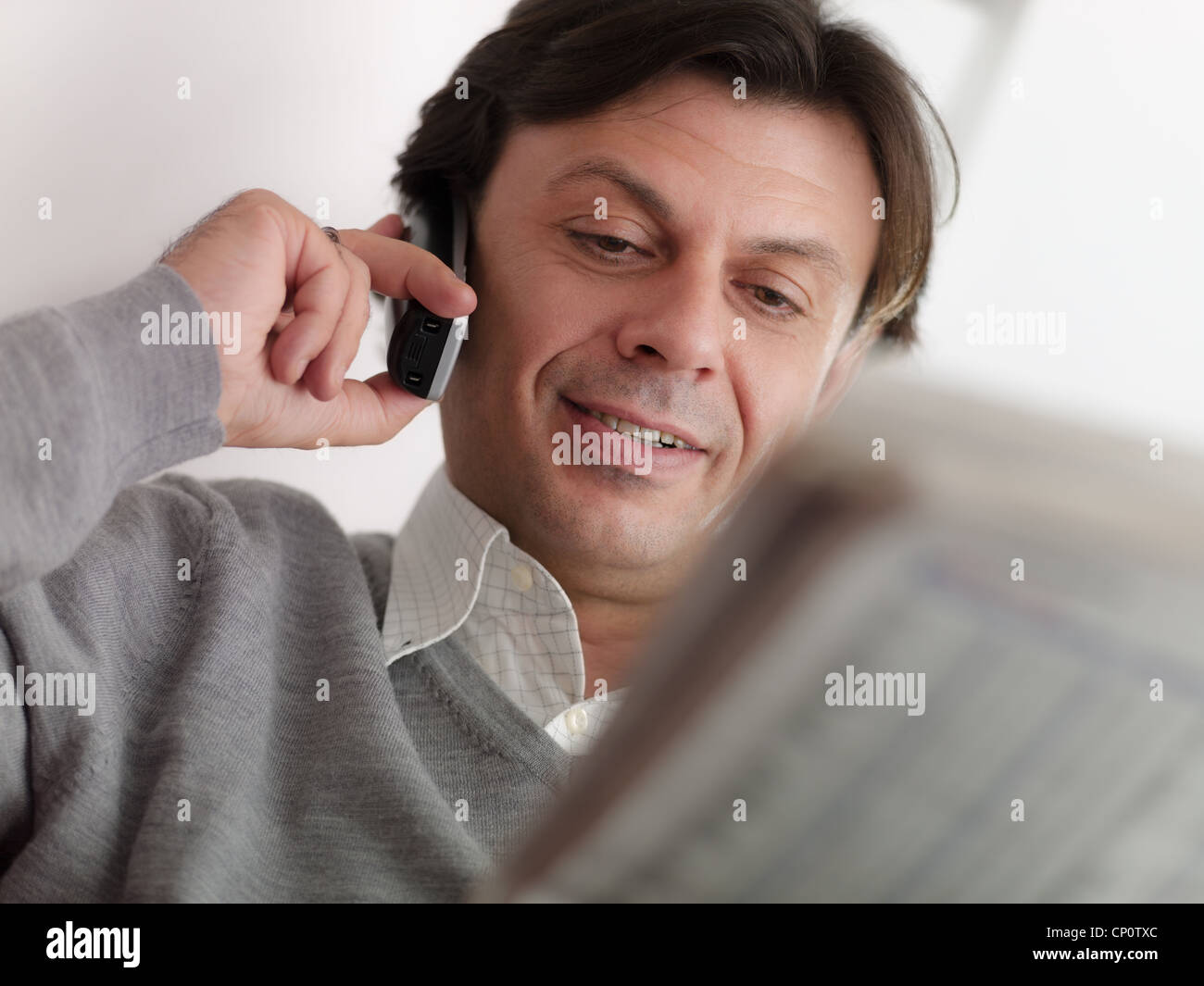 Retrato del Cáucaso feliz hombre adulto sentado en el sofá, hablando con el comerciante de cordless y comprobación de listas de valores Foto de stock
