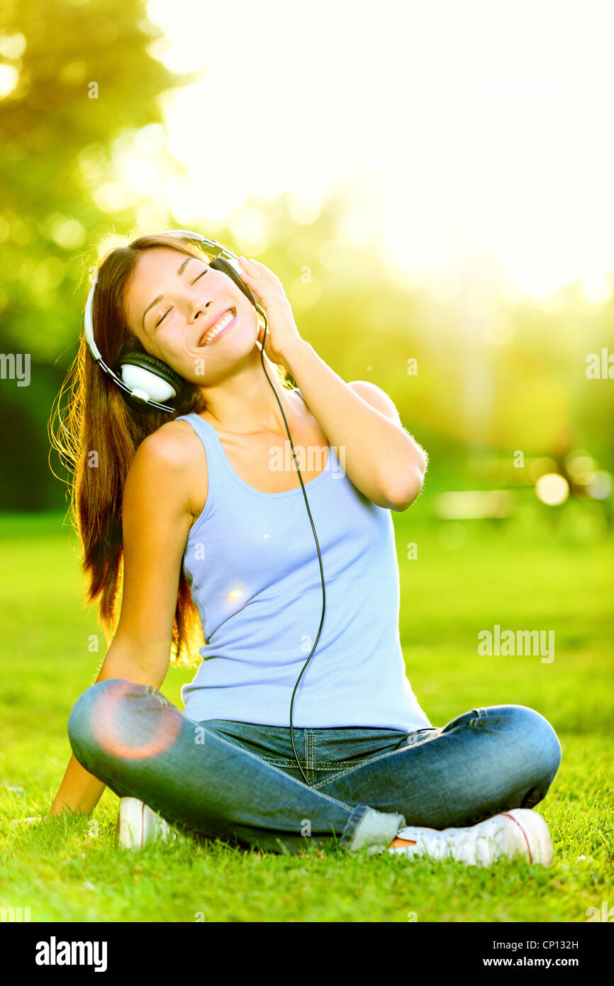 Feliz joven estudiante universitario mixto de Asiáticos y Caucásicos etnicidad en park disfruta de la música en los auriculares Foto de stock