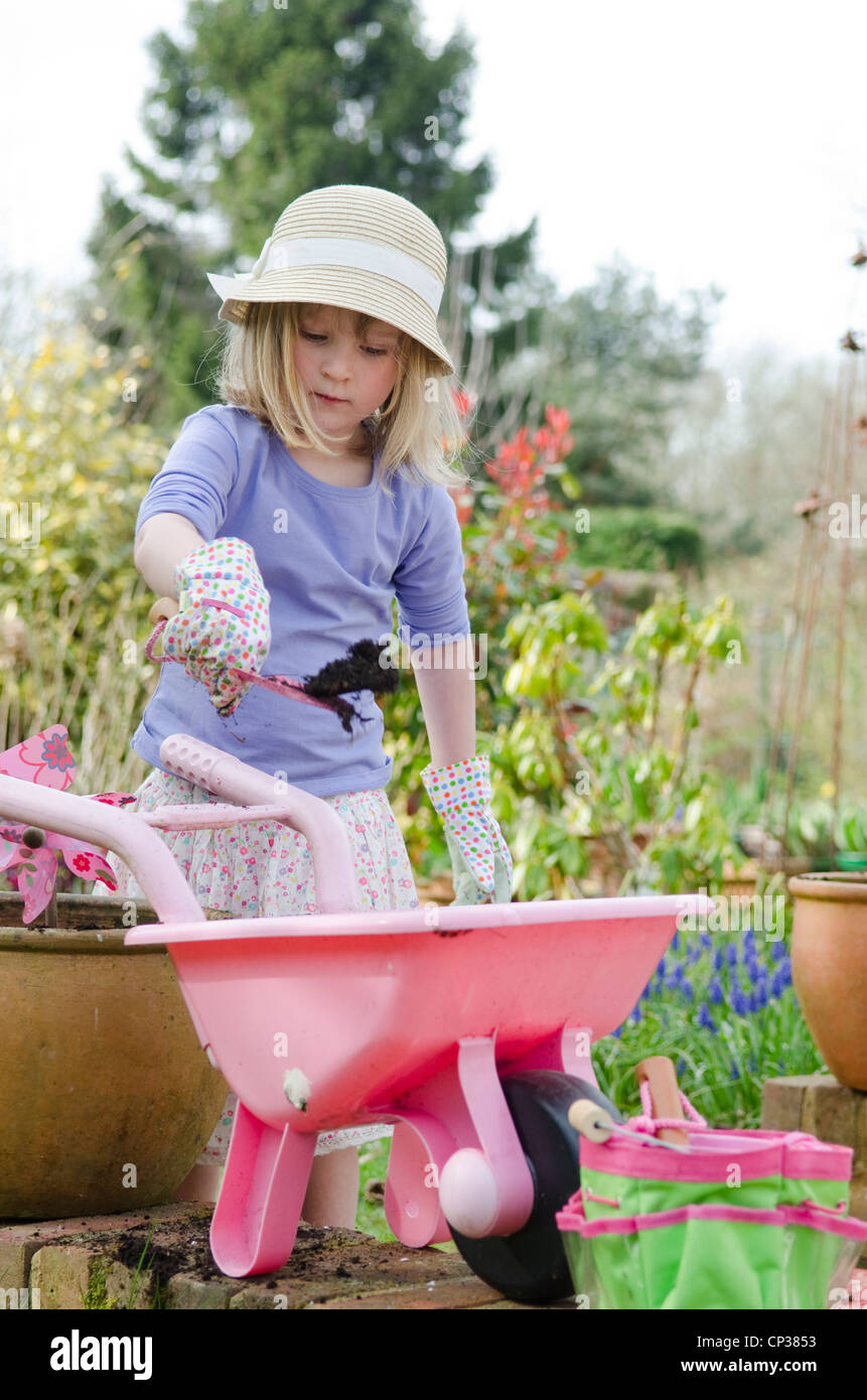 Cuatro años de edad, niña jugando en el jardín con guantes, espátula, carretillas y ollas. Foto de stock