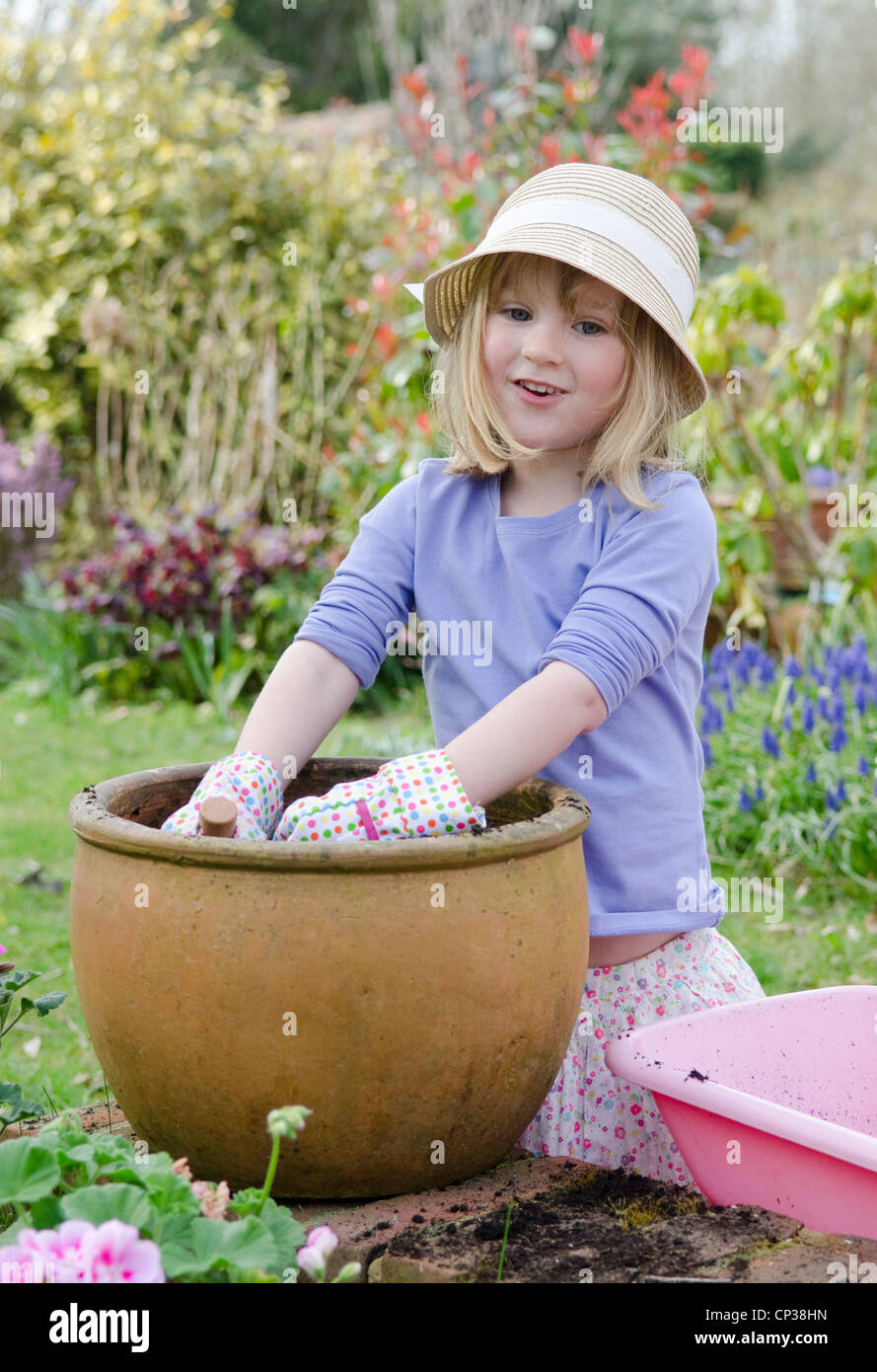 Cuatro años de edad, niña jugando en el jardín con guantes, espátula, carretillas y ollas. Foto de stock