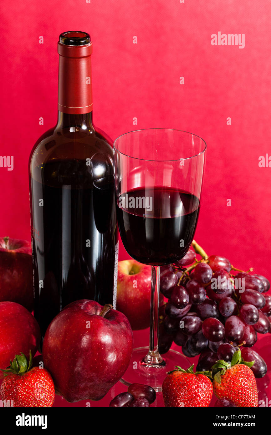 Botella de vino rojo y rojo vino en cristal con rojas manzanas, uvas y fresas. Foto de stock