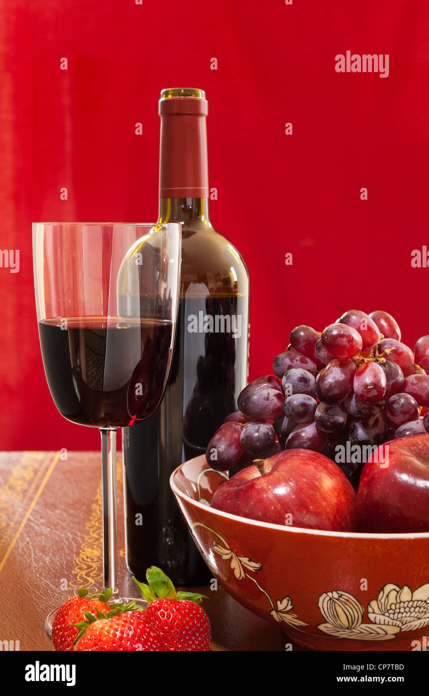 Botella de vino rojo y rojo vino en cristal con rojas manzanas, uvas y fresas. Foto de stock