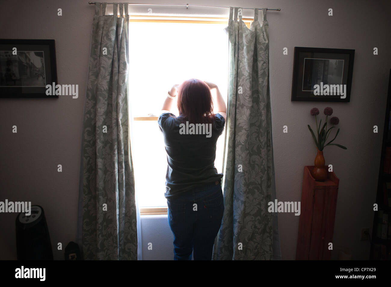 Mujer de mediana edad de pie delante de la ventana de la habitación mirando afuera. Foto de stock