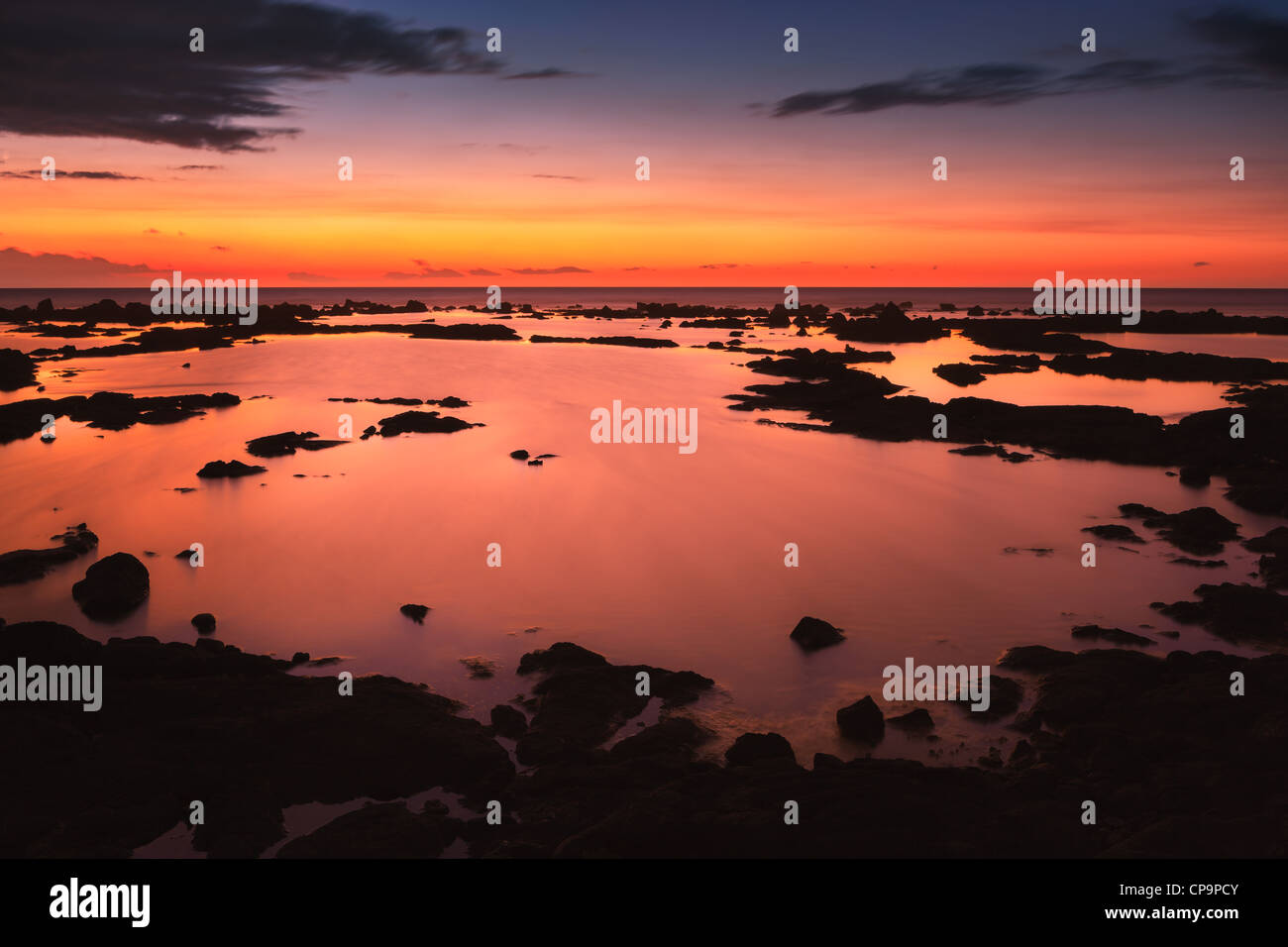 Puesta de sol en el Pacífico con rocas de lava en primer plano. Foto de stock