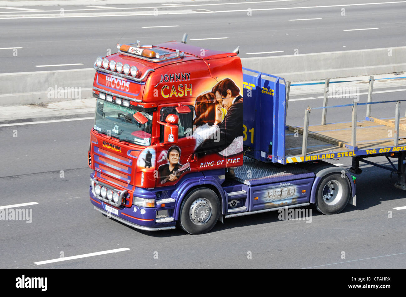 Unidad de tractor con cabina de camión Scania lateral y delantera Con Johnny Cash gráficos y cama plana remolque de conducción a lo largo Autopista del Reino Unido carretera Inglaterra Foto de stock