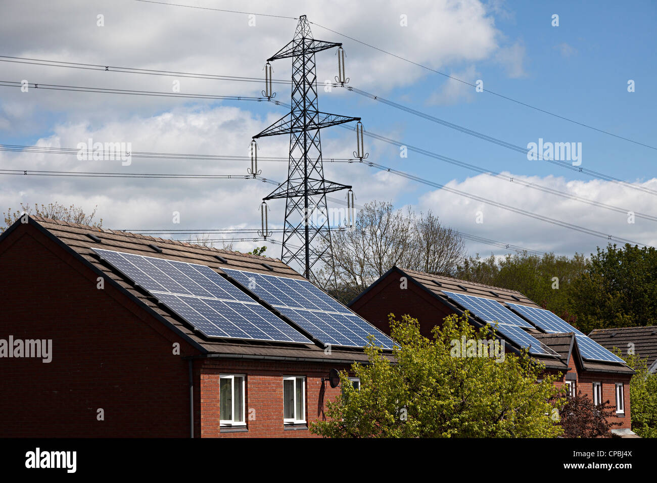 Paneles solares en viviendas con torres eléctricas detrás, Wales, REINO UNIDO Foto de stock