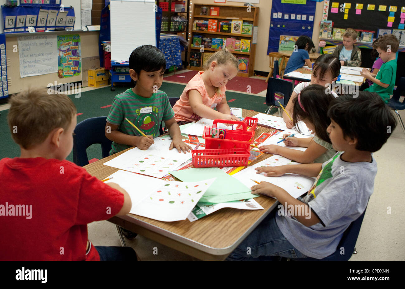 Grupo multiétnico de los estudiantes de kindergarten en una gran mesa de trabajo en el aula de la escuela primaria pública de Texas Foto de stock