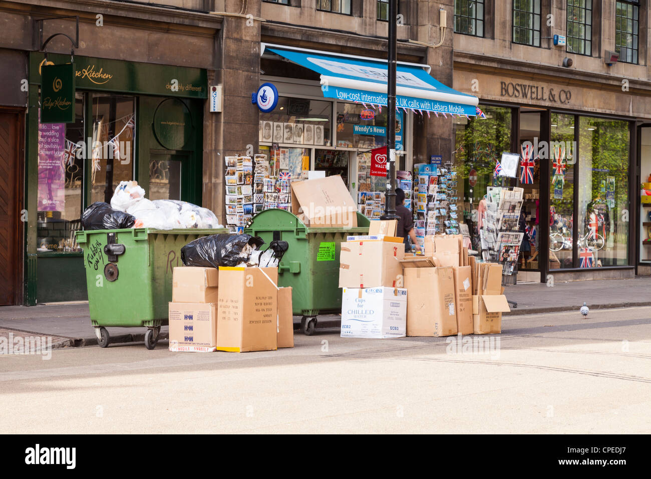 Dos saltos y varias cajas de basura o basura esperando en el bordillo de la acera para su recogida, en Broad Street, Oxford, Inglaterra. Foto de stock