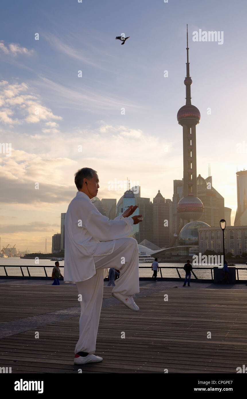 Hombre en blanco uniforme haciendo ejercicios de tai chi en el Bund al amanecer con Pearl Tower en Shanghai China Foto de stock