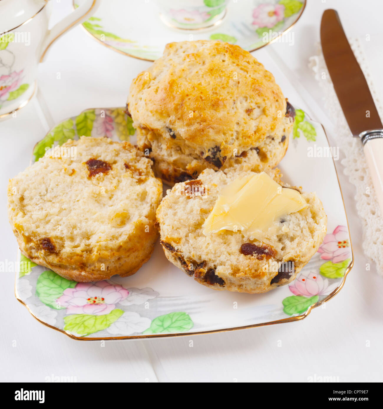 Fecha dos scones con mantequilla y una taza de té, dispuestas en hermosa vajilla antigua. Foto de stock