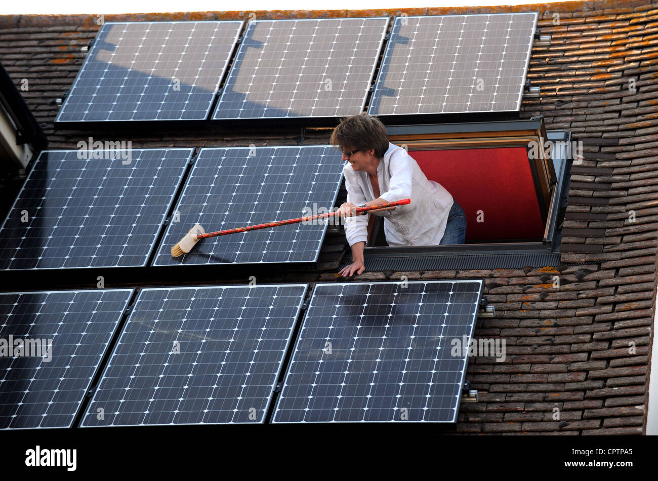 Mujer de limpieza de polvo sus paneles solares en el techo con una escoba  de hogar Sussex, UK Fotografía de stock - Alamy