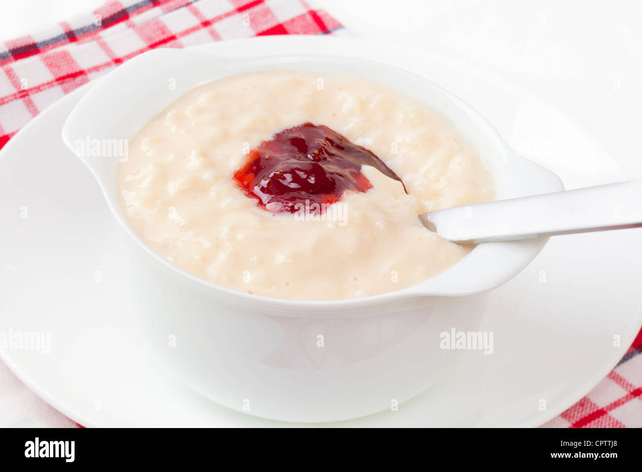 Un tazón de arroz con leche, coronado con mermelada de fresa, excavando en la cuchara. Foto de stock