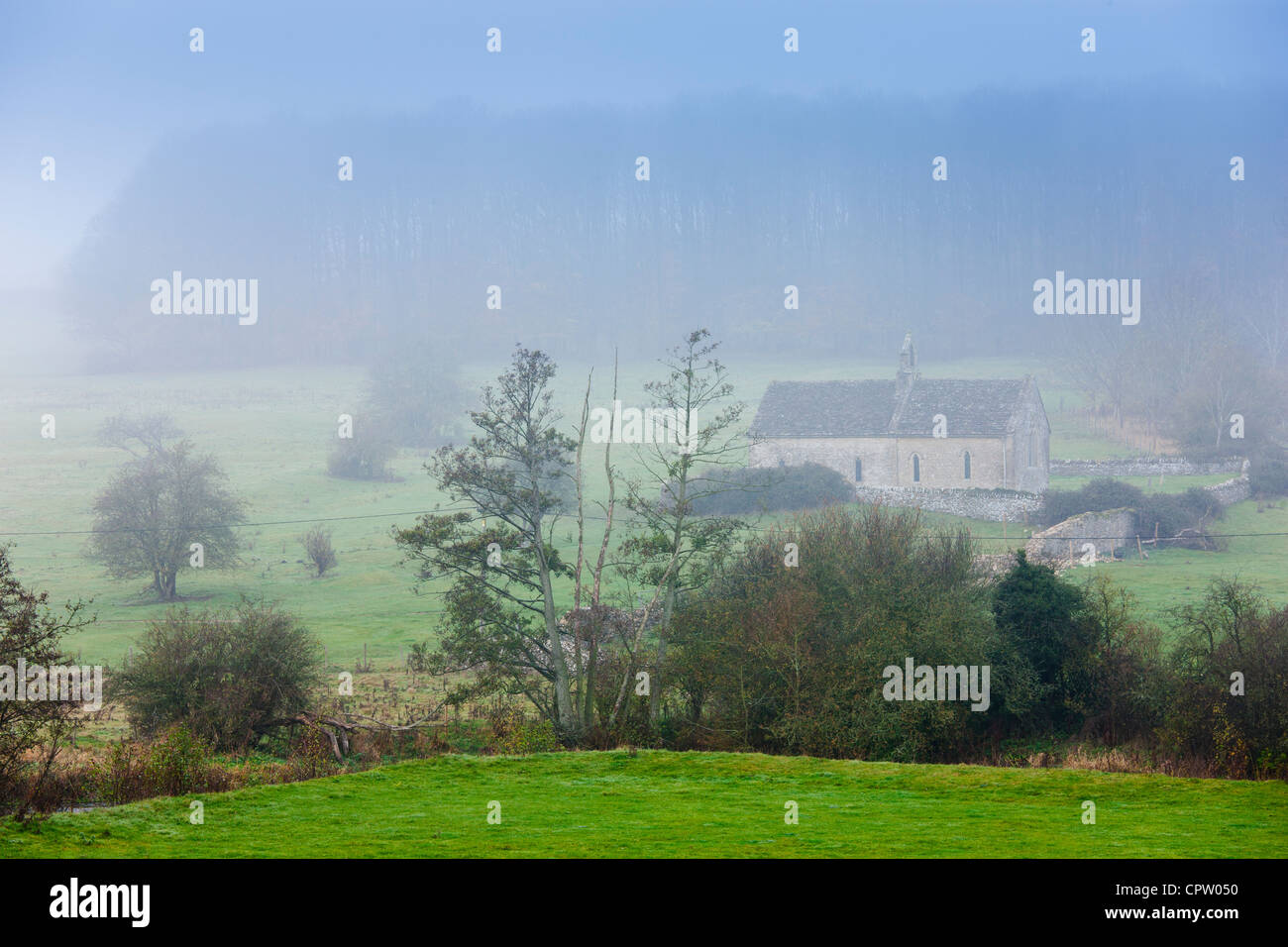 Misty escena y la iglesia de St Oswald, una capilla remota en un campo, en Widford cerca de Burford en Cotswolds, Oxfordshire, REINO UNIDO Foto de stock