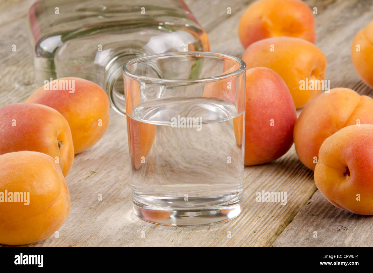 Aguardiente de fruta en un vaso y albaricoques frescos en el fondo Foto de stock
