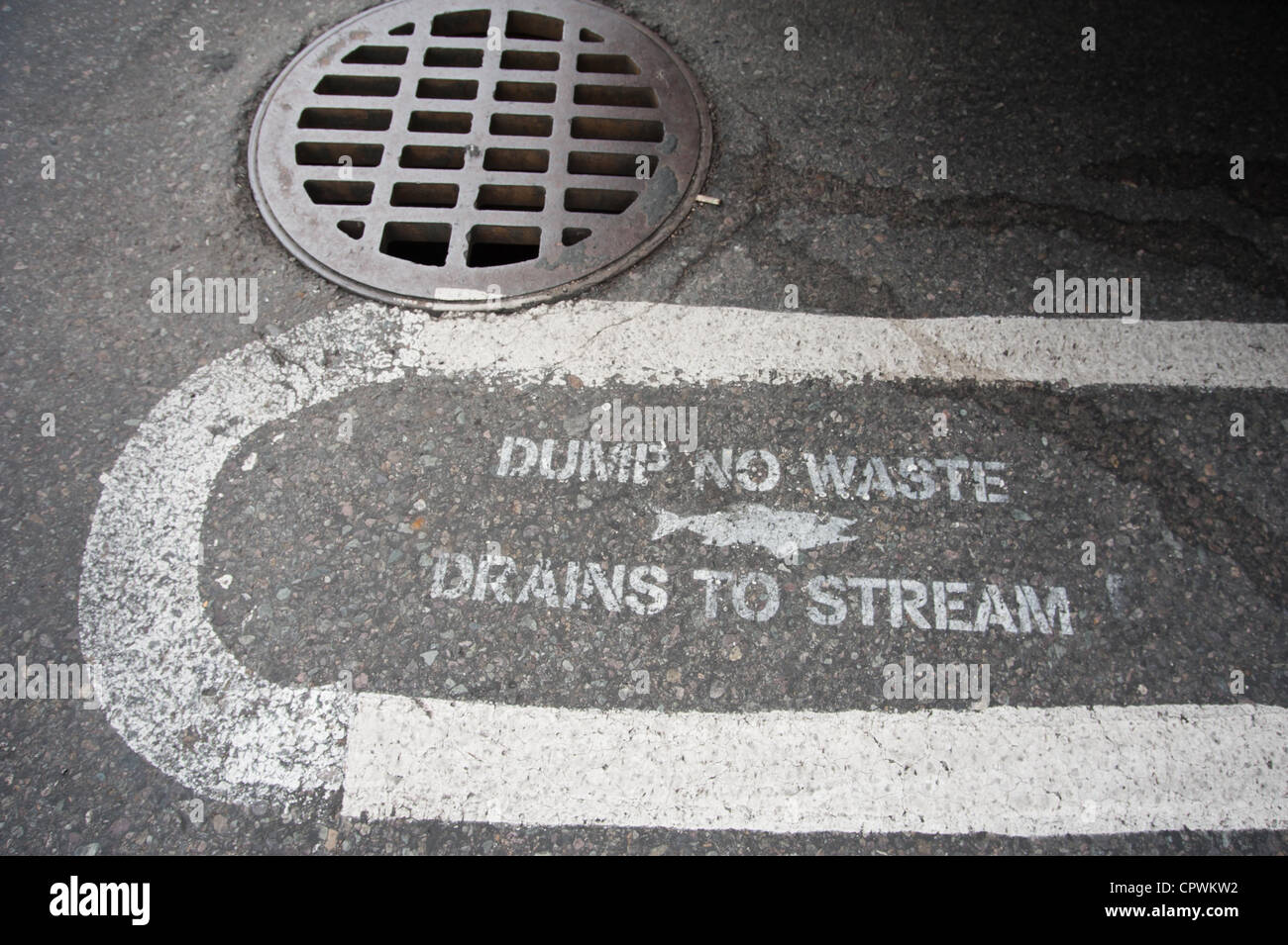 Un señales pintadas en el pavimento advierte a la gente no verter los desechos en el drenaje se drena en el arroyo cercano. Foto de stock