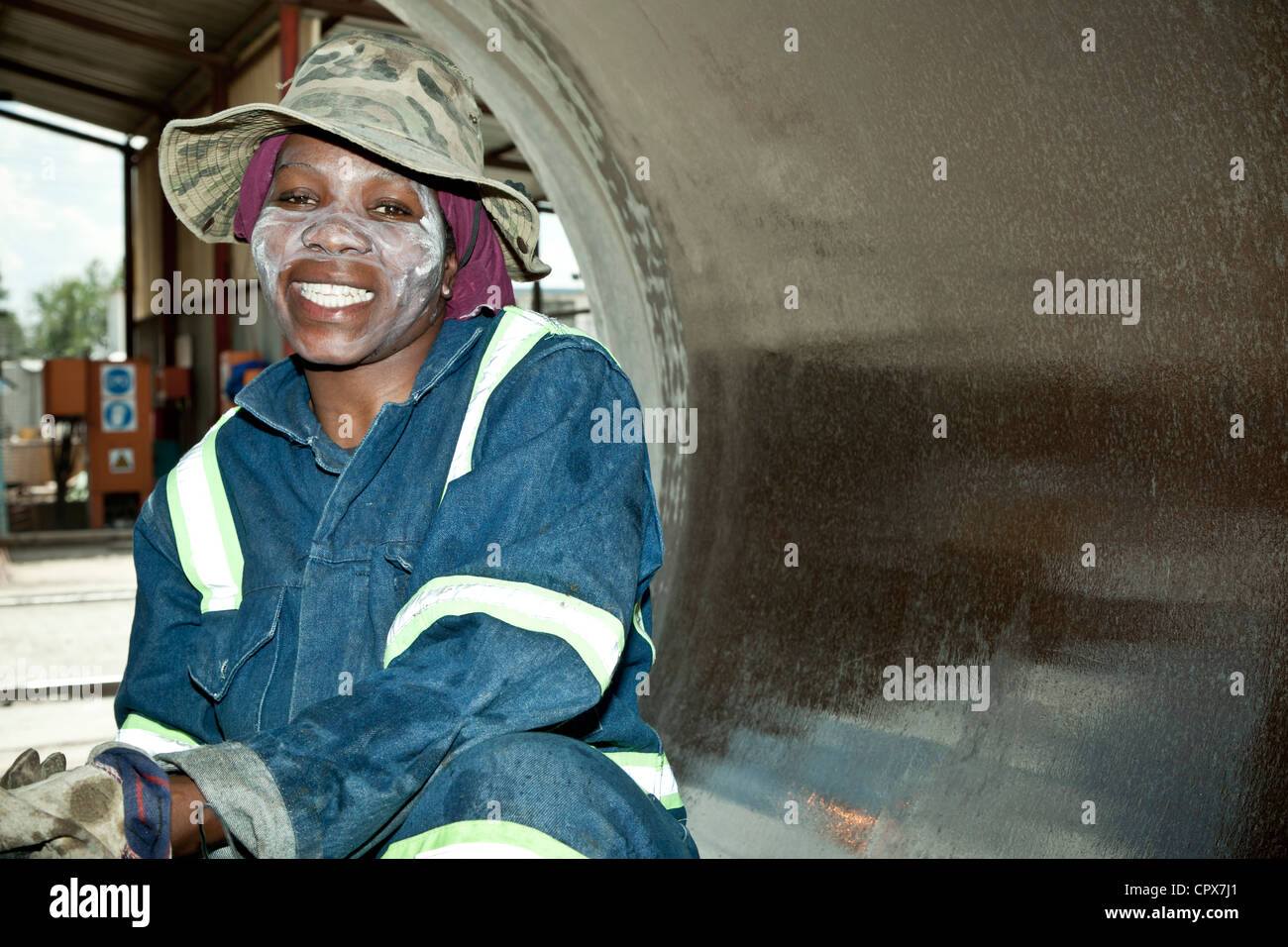 Hembra negro trabajador de fábrica limpia el interior de un tubo grande, sonriendo Foto de stock