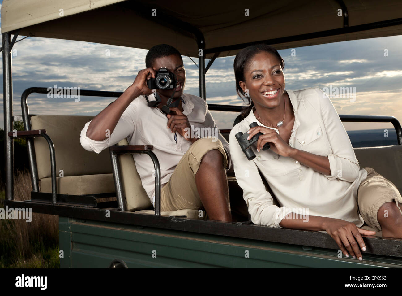 Una pareja africana sentados en un juego de visualización vehículo buscando animales y tomar fotografías Foto de stock