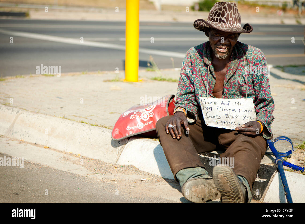 Foto de un hombre sin hogar africano sentado junto a una carretera Foto de stock
