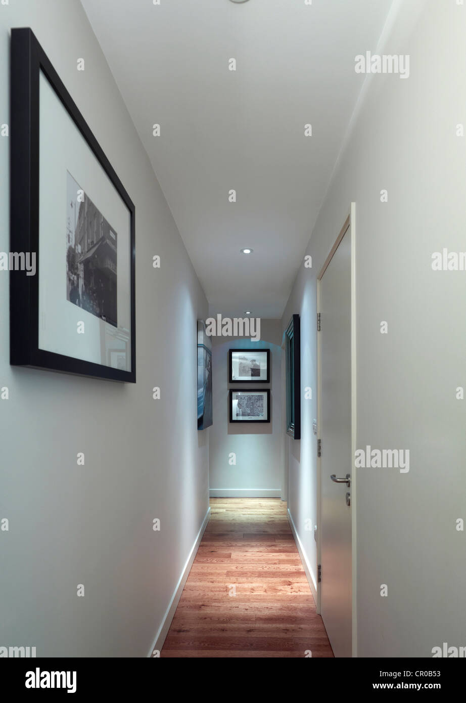 Un largo pasillo con suelo de madera y paredes blancas con cuadros que cuelgan Foto de stock