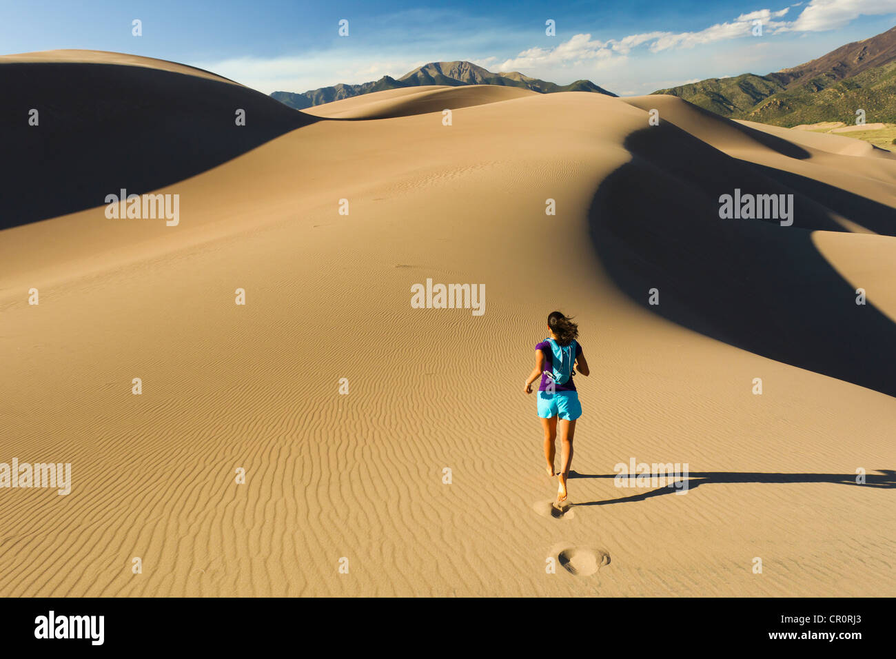 La mujer hispana ejecutándose en una duna de arena Foto de stock
