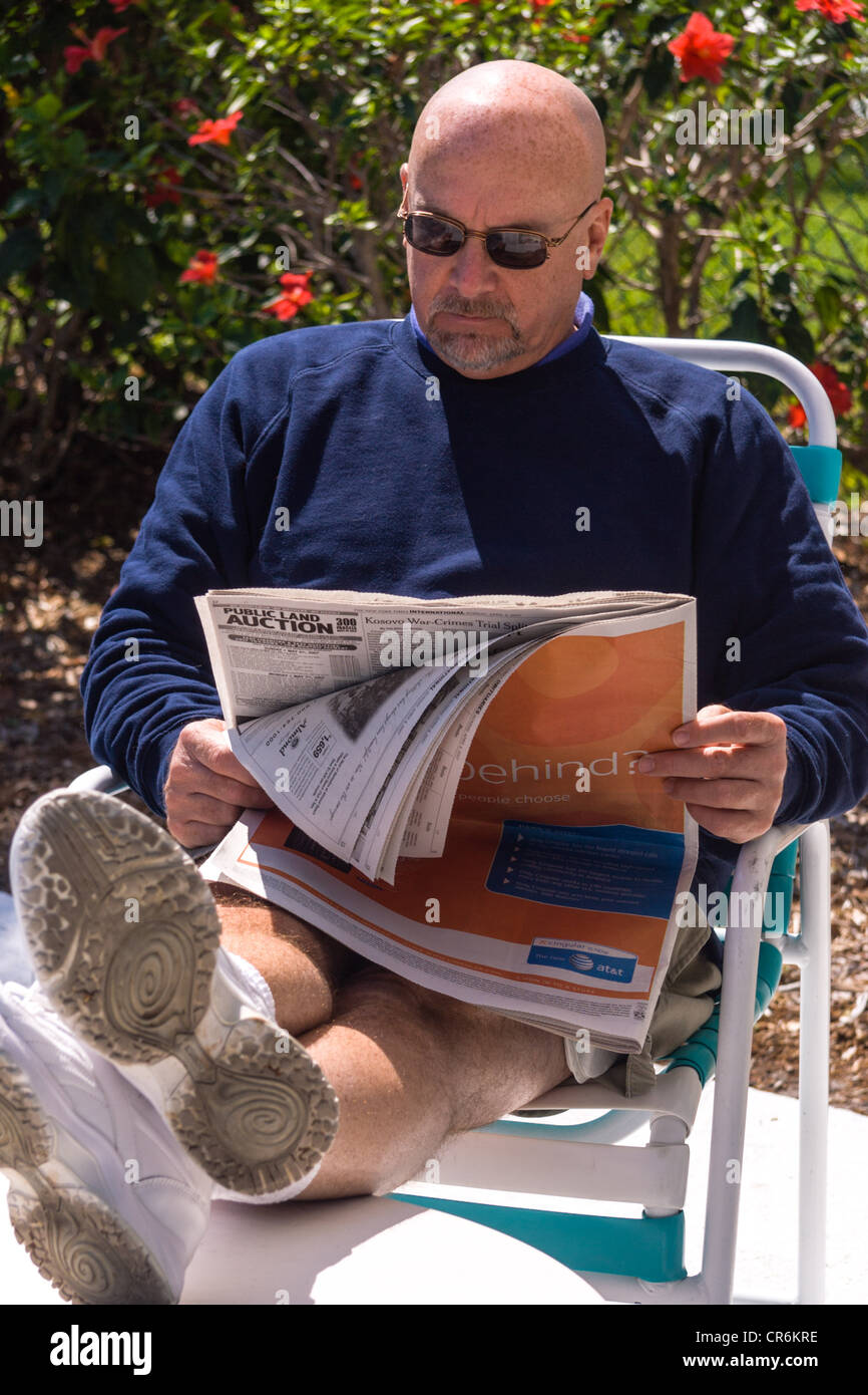Hombre Calvo sentado al sol, leyendo un periódico en el exterior Foto de stock