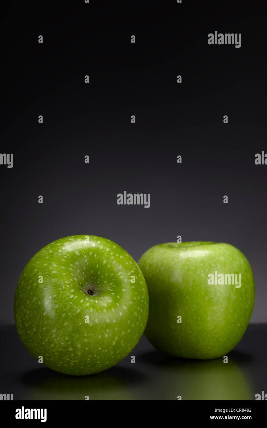 Dos manzanas Granny Smith verde sobre una placa de cristal oscuro Foto de stock