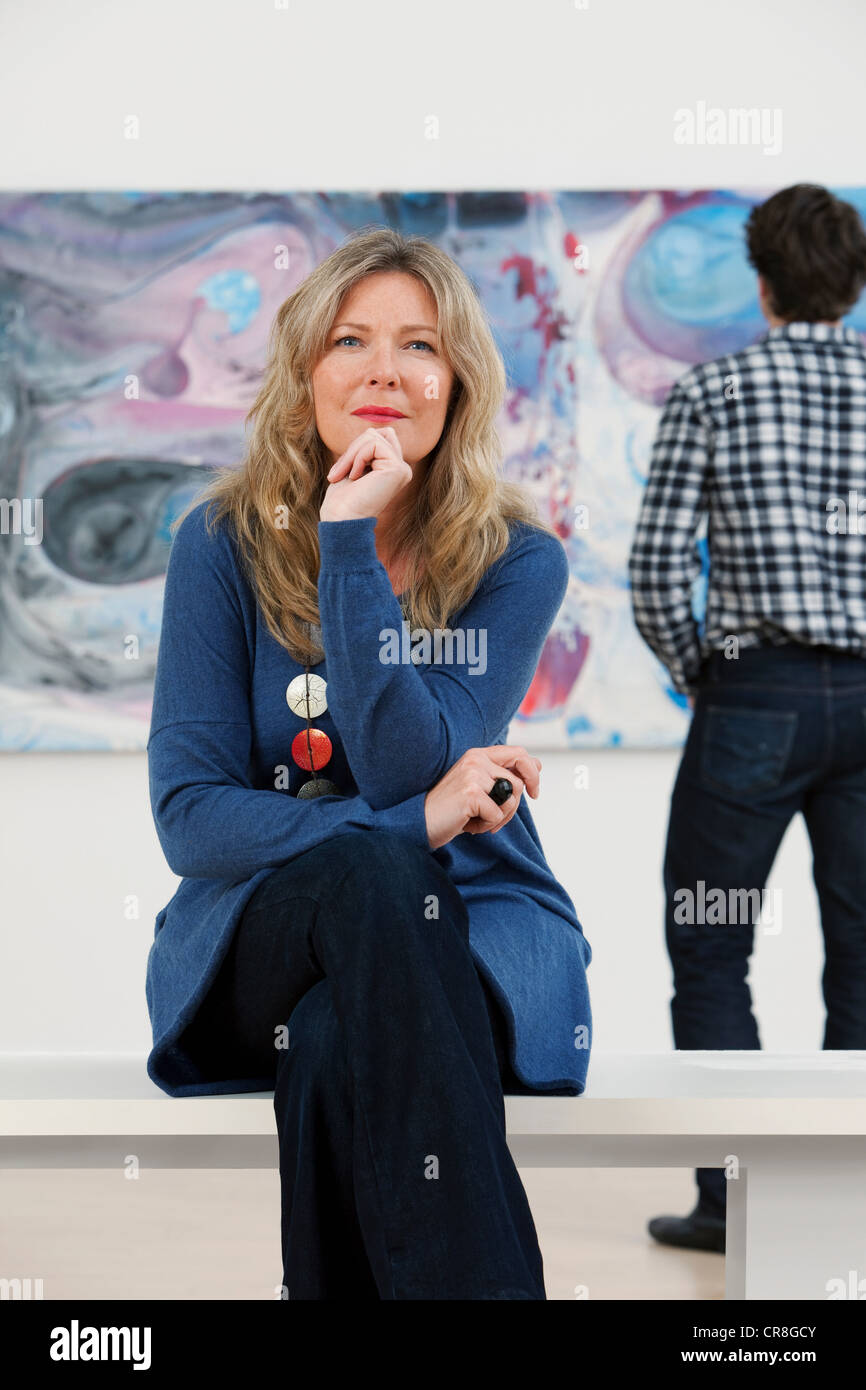 Mujer adulta media sentado delante de óleo en la galería Foto de stock