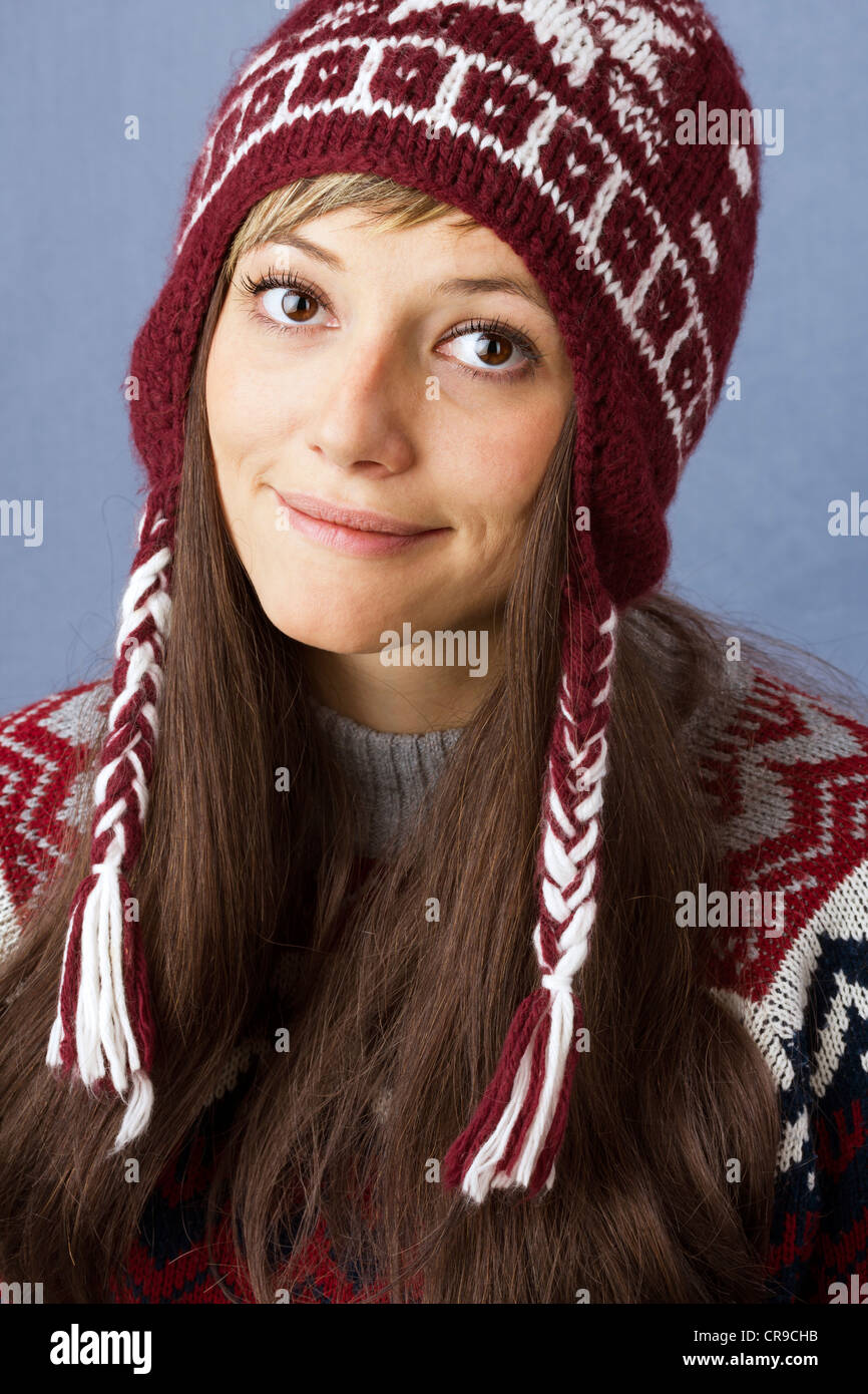 Bastante joven con una ligera sonrisa vestir lana gorro con patrón de Noruega. Retrato de estudio contra un fondo azul claro Foto de stock