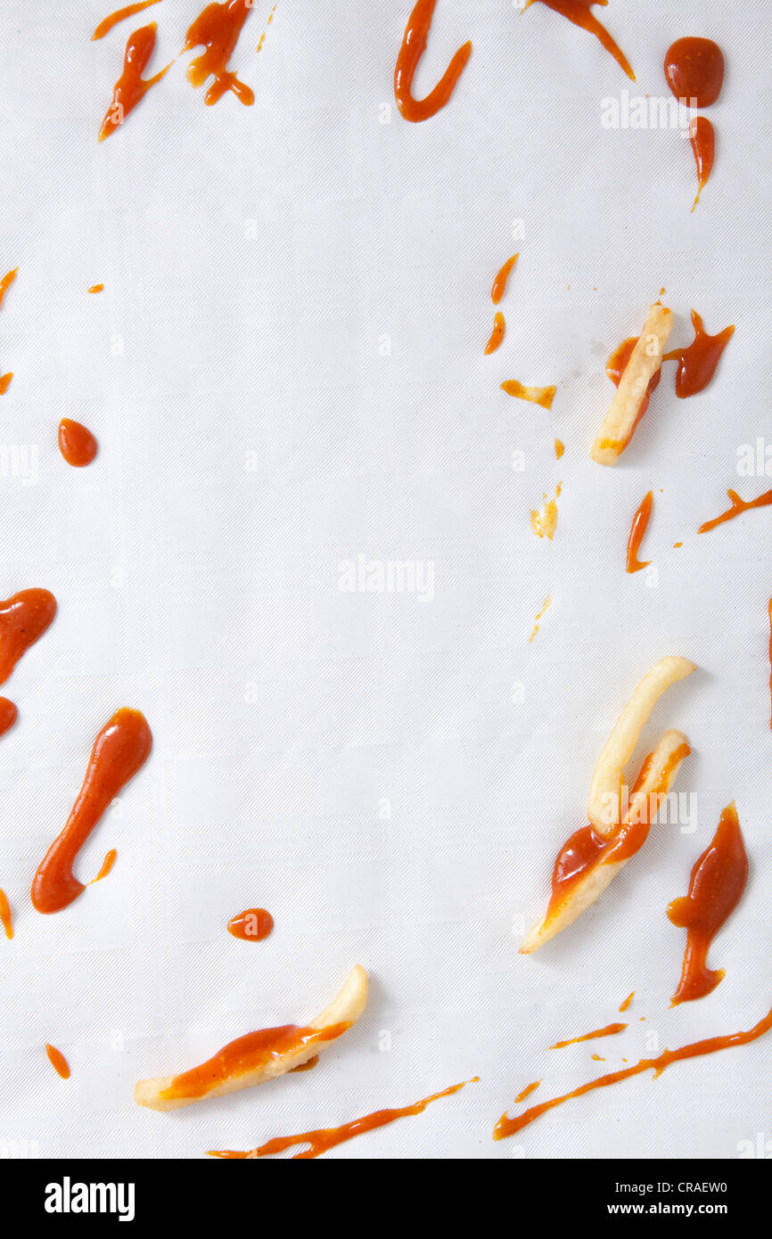 Patatas fritas y ketchup derramado sobre un mantel de papel, restos de comida Foto de stock