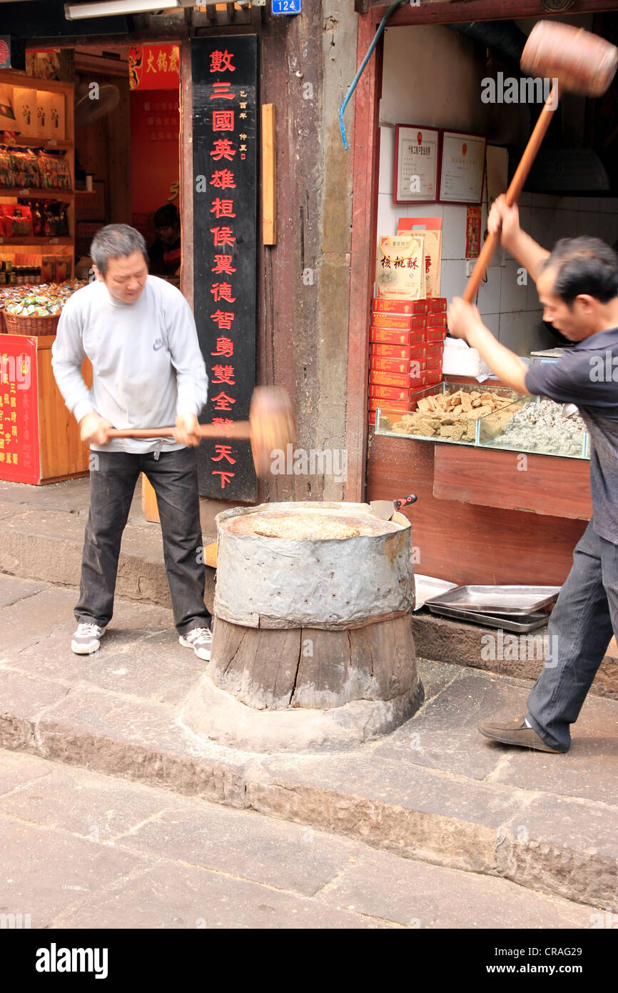 Dos hombres chinos martilleo jengibre pasta en el proceso de elaboración de dulces. Foto de stock