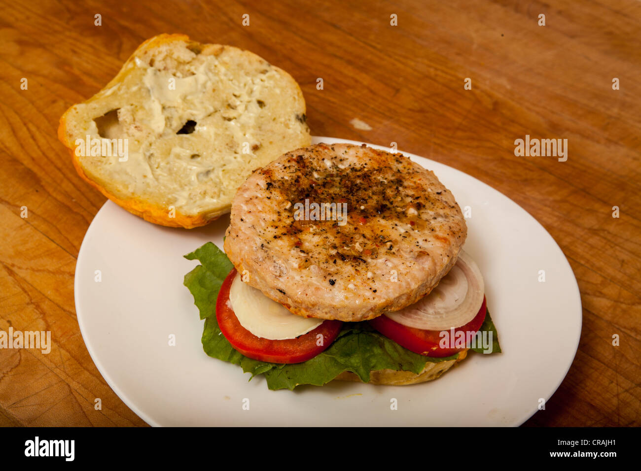 Una hamburguesa de Turquía sobre un bagel de jalapeño y queso con cebolla y tomate sobre una cama de lechuga romana Foto de stock