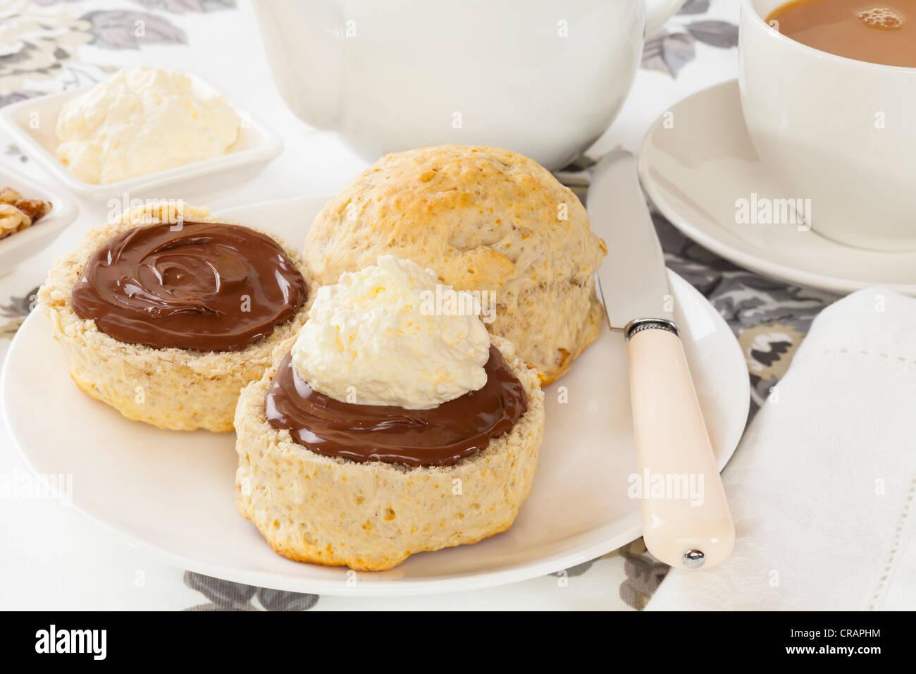 Nogal caseros scone con chocolate para untar y crema, servido con una taza de té. Foto de stock