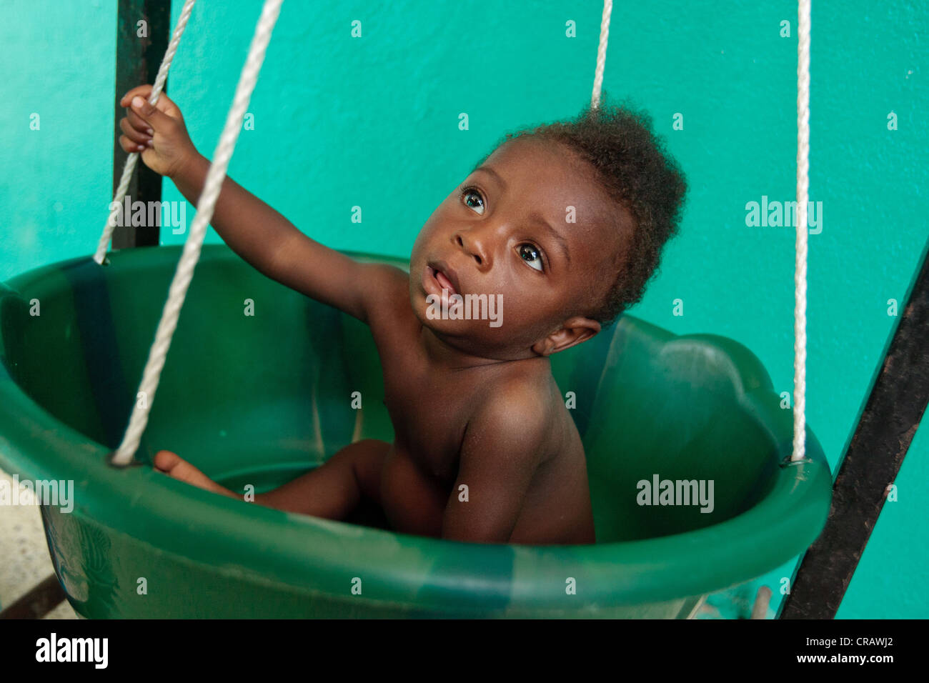 Un niño se sienta en un recipiente de plástico atado a una escala mientras se pesa en el centro de salud de canalización en Monrovia Foto de stock