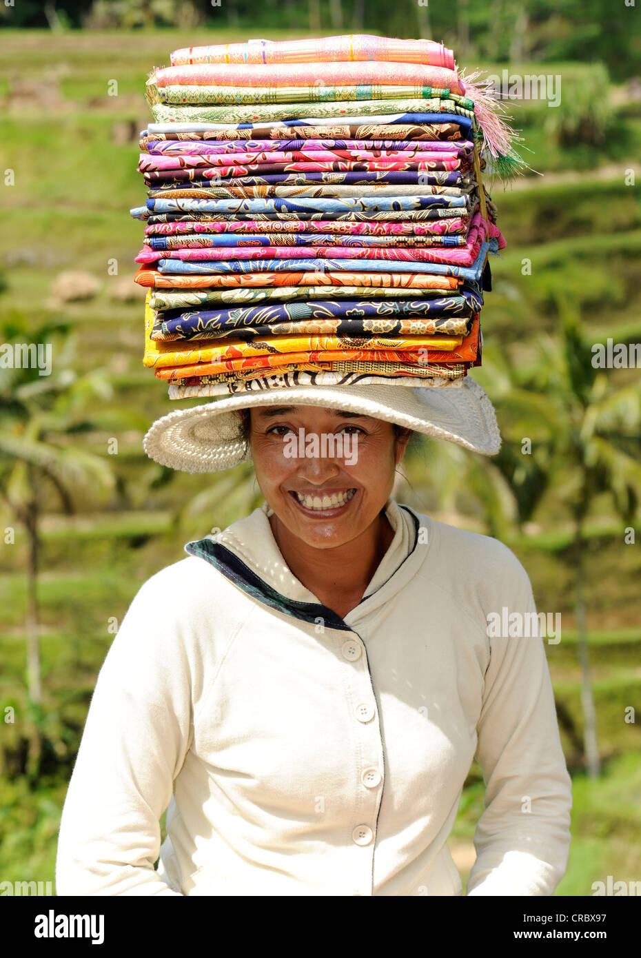 Mujer de Indonesia llevando una pila de tela de seda sobre su cabeza, Ubud, Bali, Indonesia, en el sudeste de Asia Foto de stock