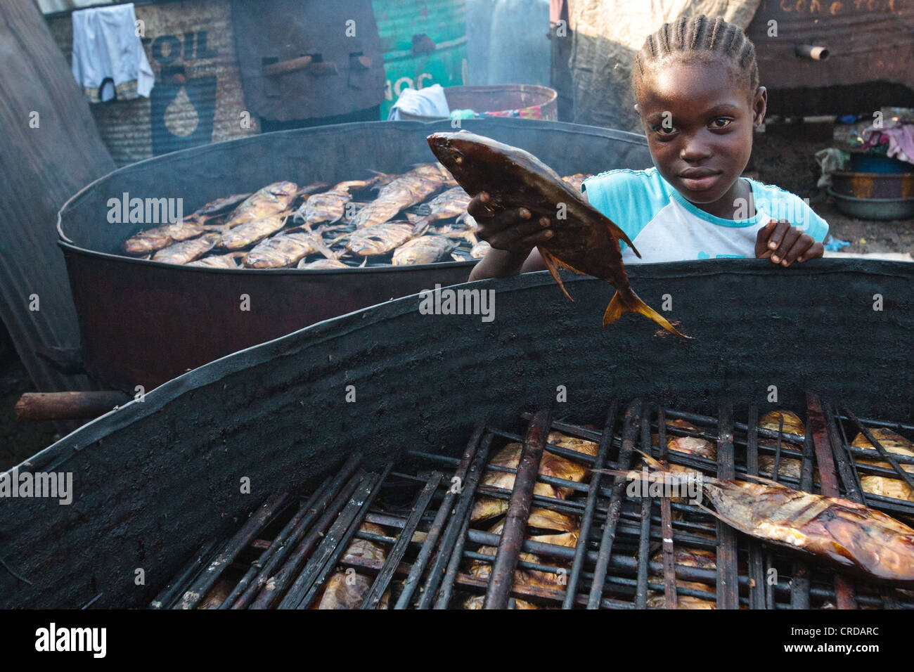 Una niña recoge un gran pescado ahumado en la barriada de West Point de Monrovia, la capital del condado de Montserrado, Liberia el lunes 2 de abril, 2012. Foto de stock