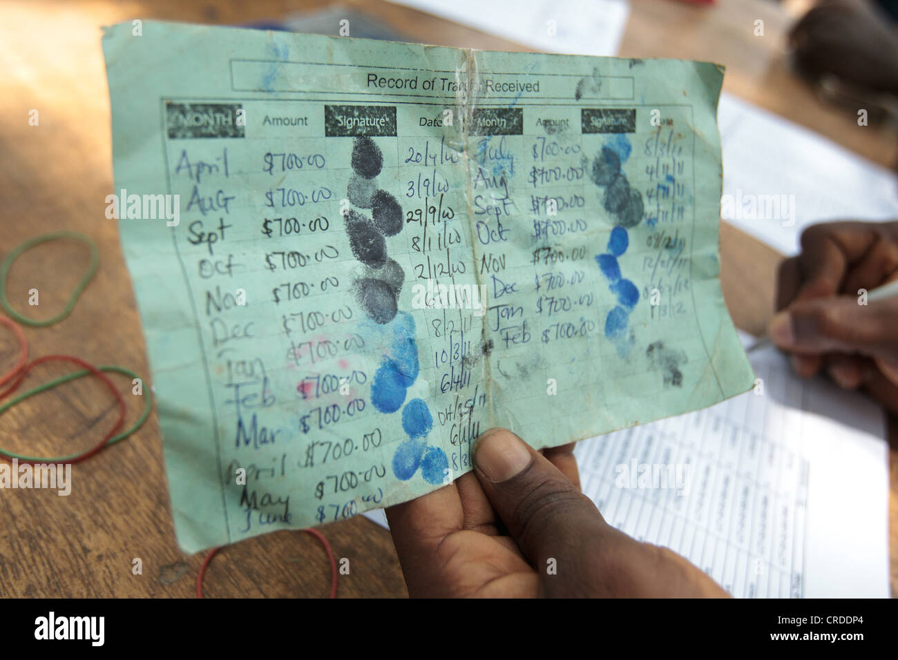 El personal del proyecto mantenga un beneficiario tarjeta durante una distribución de programas sociales de transferencias en metálico en la aldea de Julijuah, Liberia Foto de stock