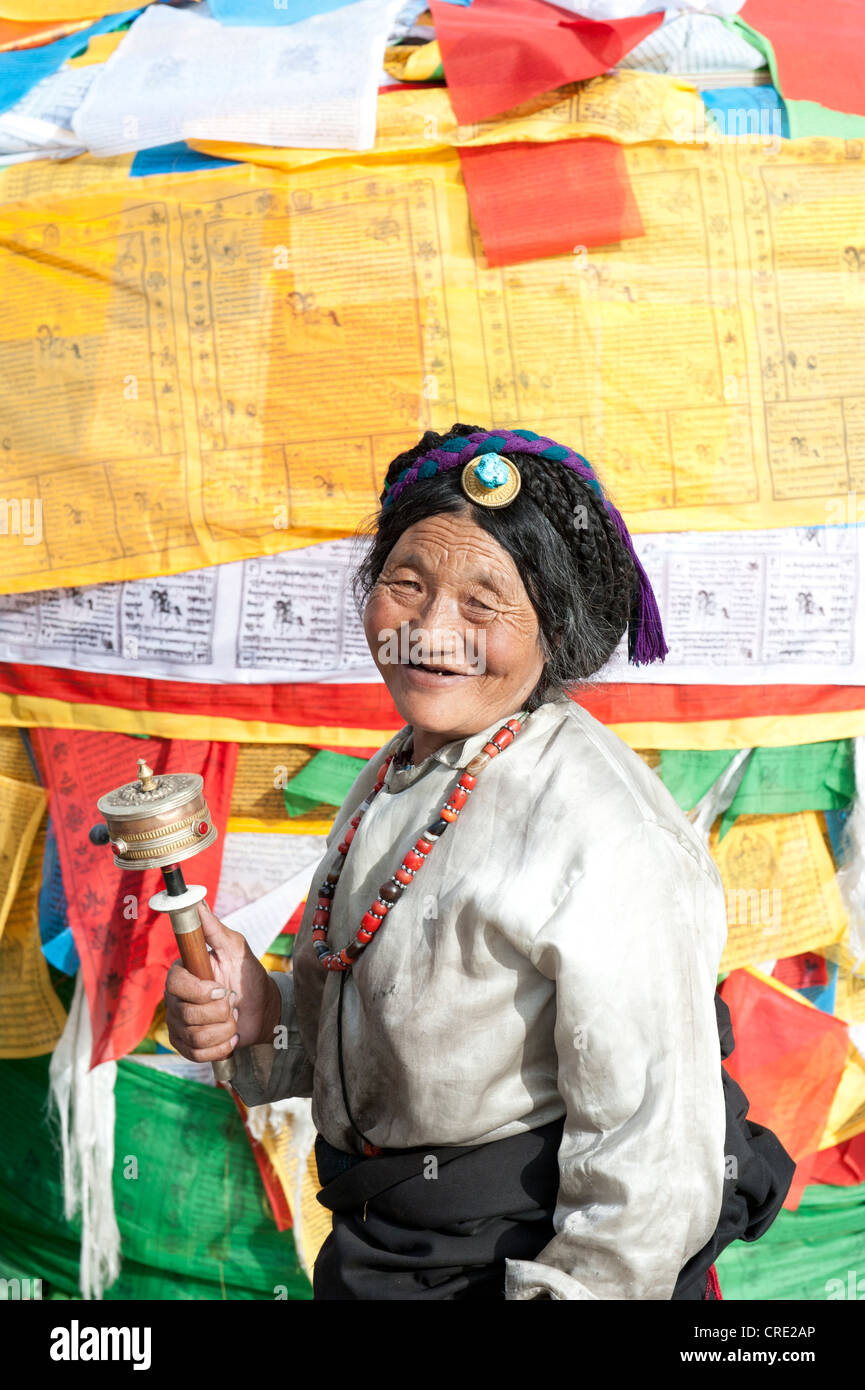 El budismo tibetano, Tibetano devota con rueda de oración delante de coloridas banderas de oración, Plaza de Barkhor, Lhasa, Himalaya, Tibet Foto de stock