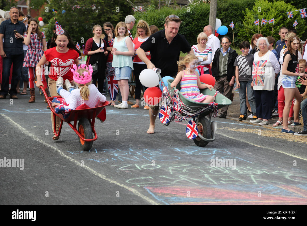 Personas que celebraban el Queen's Diamond Jubilee tomando parte en una carretilla carrera en una fiesta en la calle Surrey, Inglaterra Foto de stock