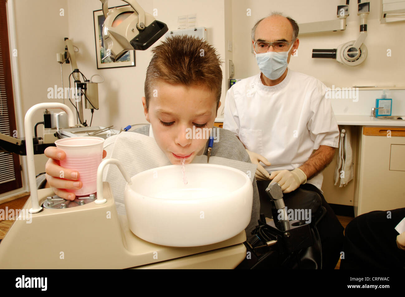 Un joven enjuague su boca con solución anti-microbiana vigilados por su dentista. Foto de stock