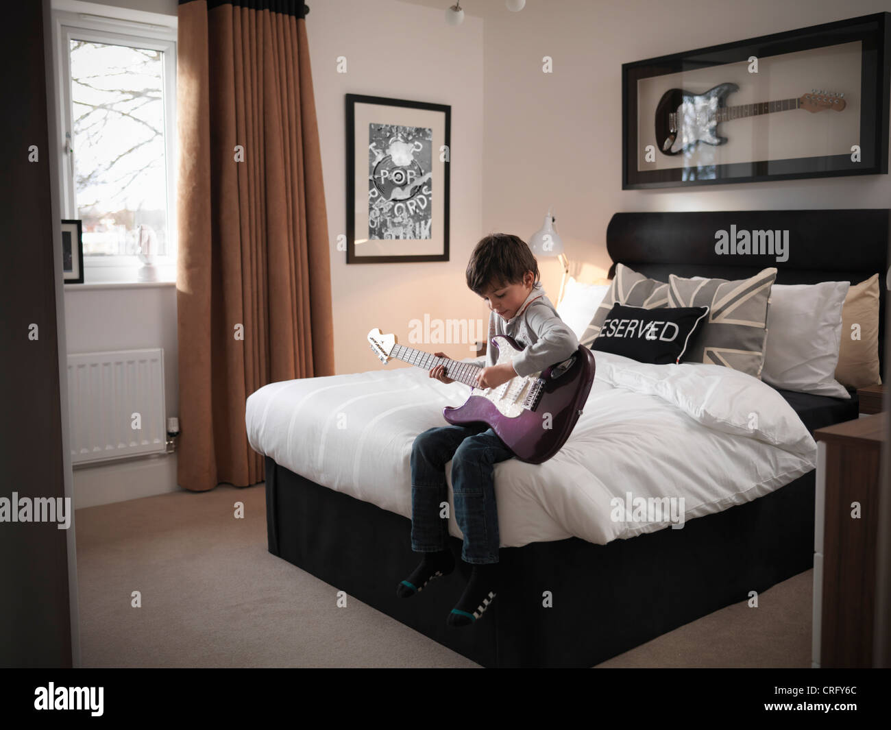 Muchacho tocando la guitarra en el dormitorio Foto de stock
