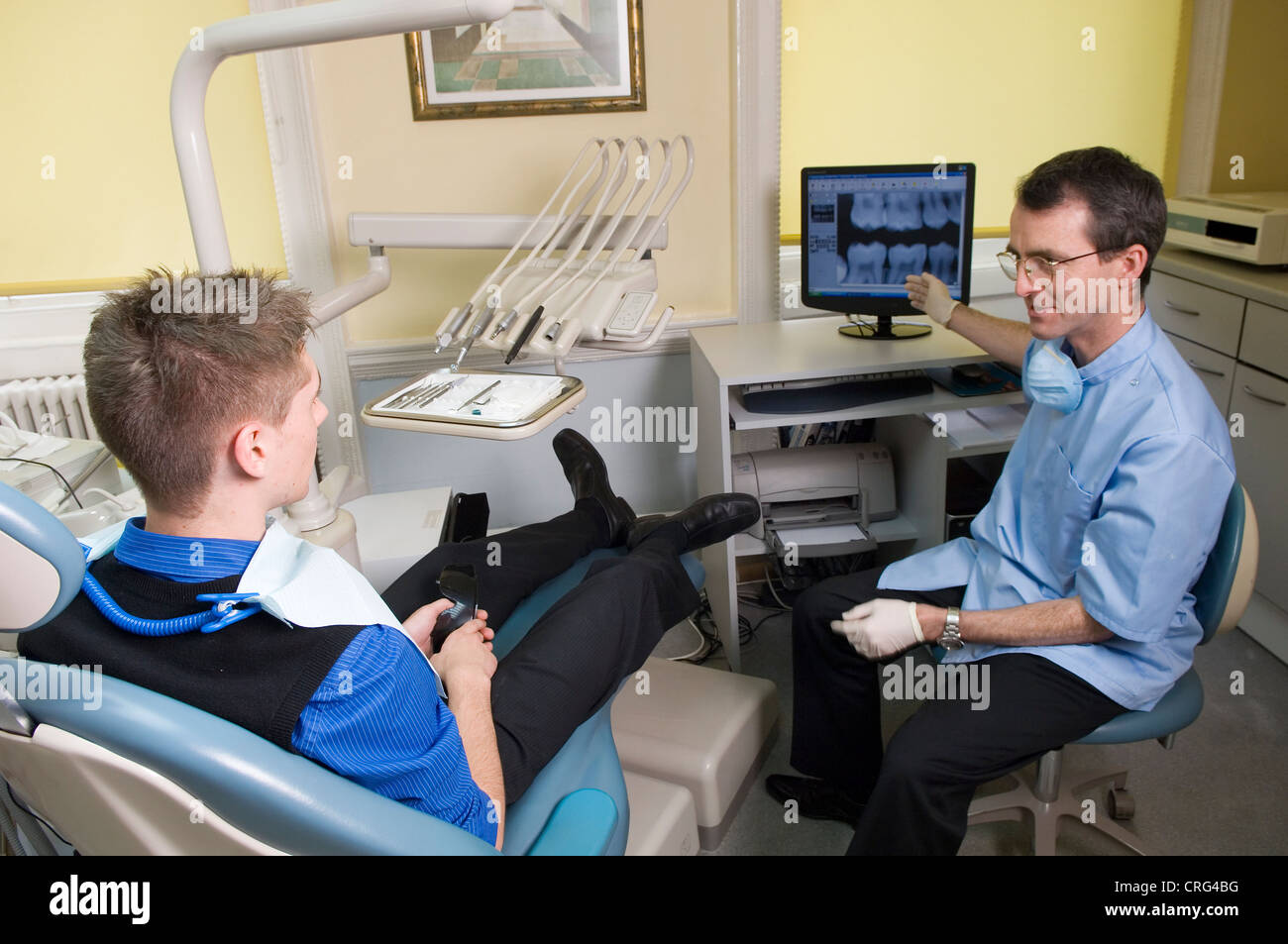 Dentista en frente de una pantalla de ordenador, analiza los resultados de un examen de rayos X con un paciente joven Foto de stock