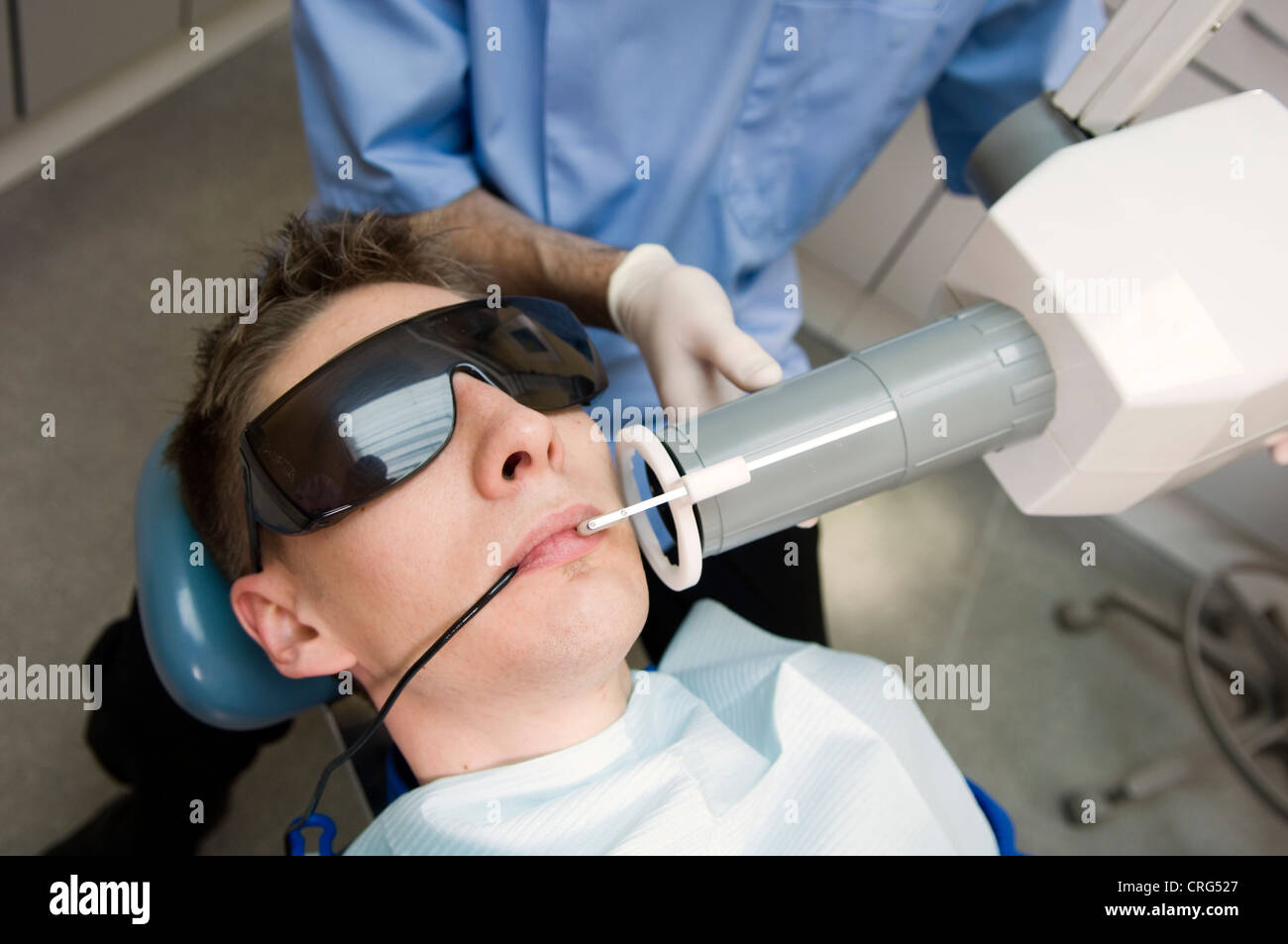 Dentista el uso de las gafas de seguridad y mascarilla de boca los rayos x de los dientes del paciente joven, también llevaba gafas de protección especial Foto de stock