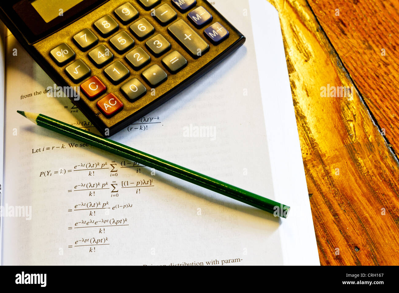 Calculadora, lápiz y matemáticas libro sobre la mesa de roble que sugieren el trabajo presupuestario o deberes. Foto de stock