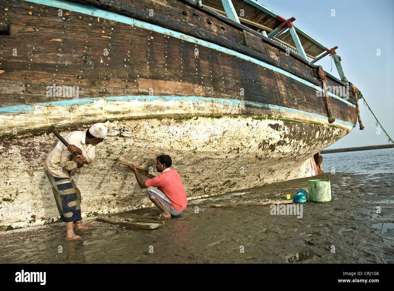 La gente local la reparación de un barco pesquero anclado en la arena, Bandar Abbas, Irán- Foto de stock